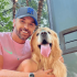 Homem branco de boné azul ao lado de um cão da raça golden retriever
